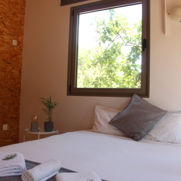 Espaço acolhedor com cama de casal e decoração simples, valorizado pela luz natural e elementos naturais.