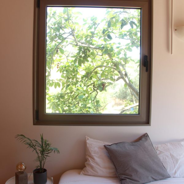Quarto com decoração clean e natural, onde uma grande janela enquadra a copa de uma árvore do lado de fora.