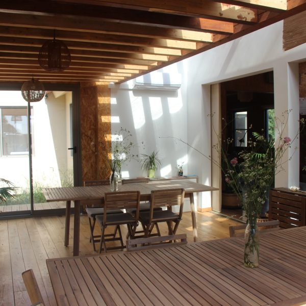 Espaço interior com mesas de madeira e decoração natural, iluminado por luz solar que entra pelas claraboias e grandes janelas.