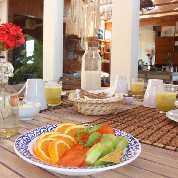 Mesa posta com frutas frescas, sumos naturais e pão artesanal num ambiente iluminado e natural, ideal para um início de dia saudável e tranquilo.