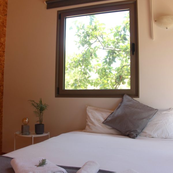 Quarto simples e luminoso, com destaque para o contacto visual direto com a vegetação exterior através da janela.